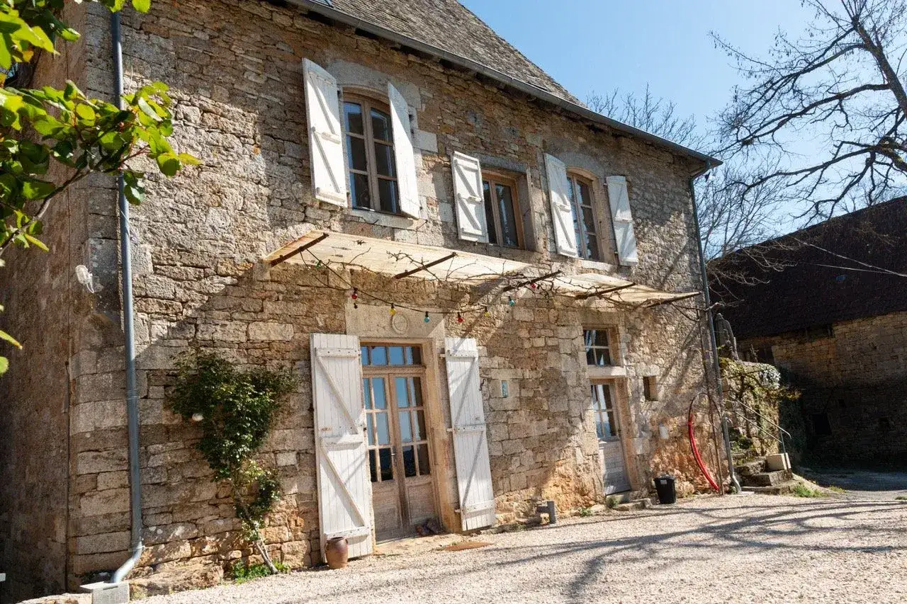 Charmante maison tradi pierre à Saint-Junien, avec volets blancs ouverts et guirlande lumineuse au-dessus de la porte.