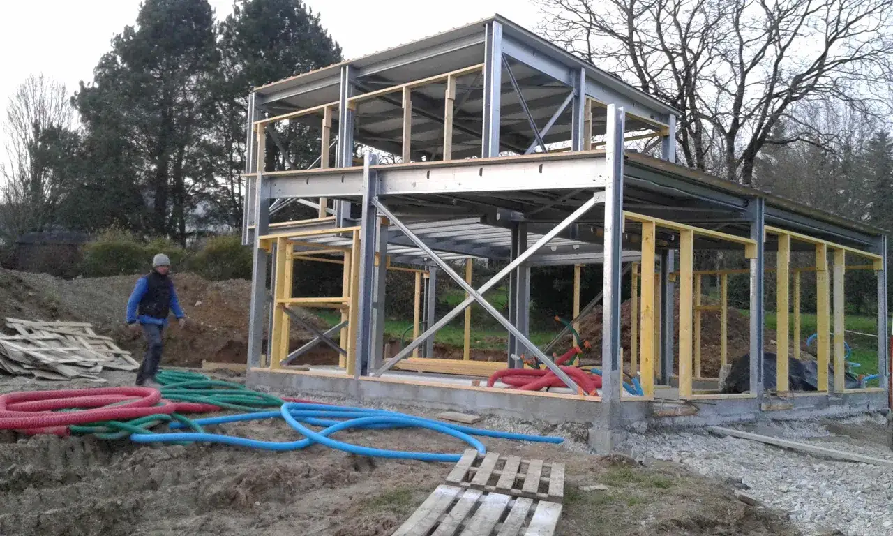 Chantier d'une maison ossature métallique. Le prix de ce type de construction est compétitif. Des tuyaux colorés sont visibles au sol.
