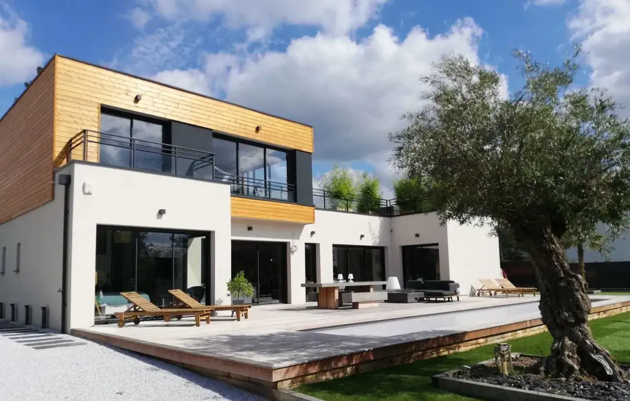 Maison moderne avec un style architectural audacieux, mêlant bois et blanc. Terrasse spacieuse avec mobilier extérieur et piscine.