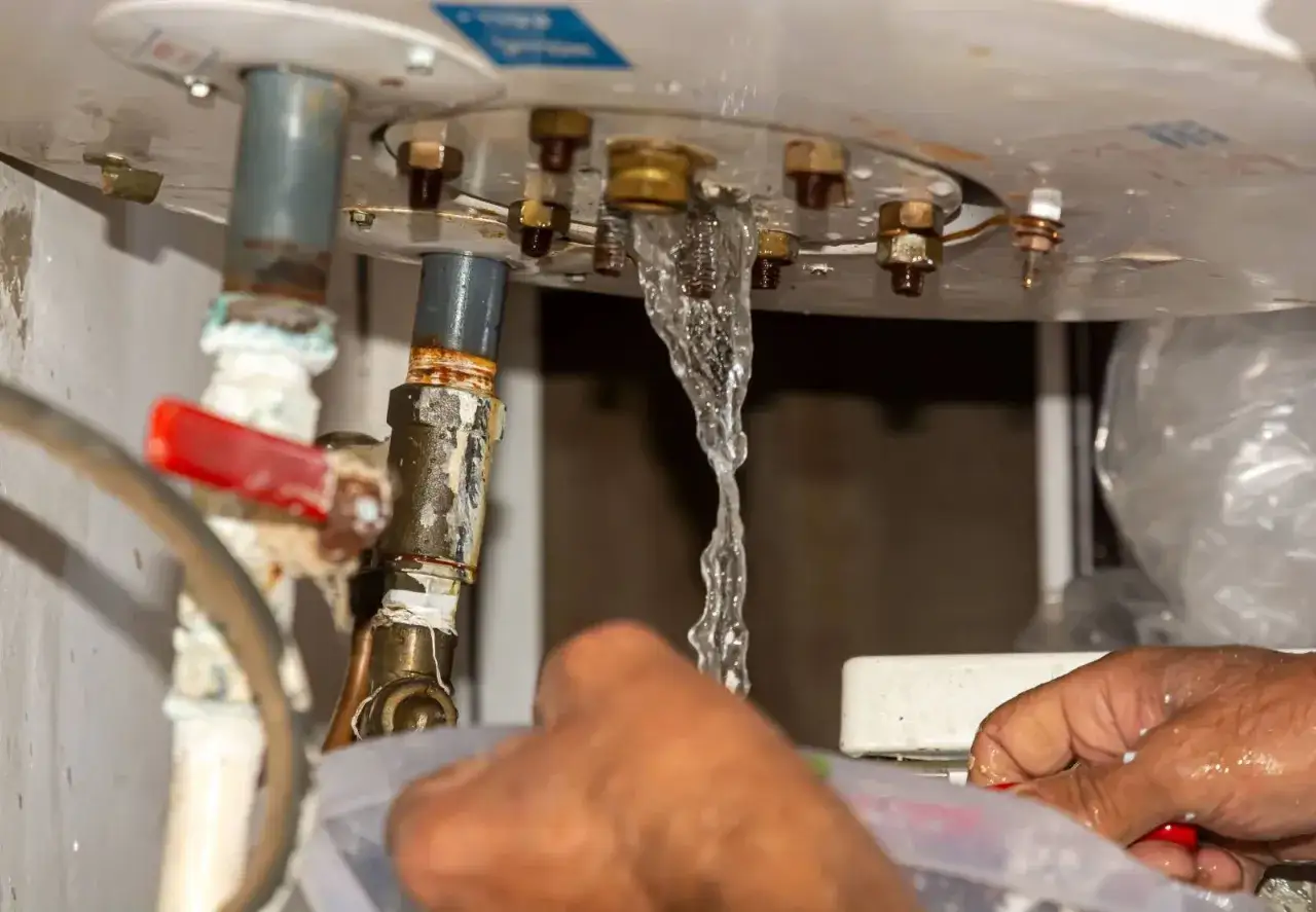 Un cumulus qui fuit par le haut d'un chauffe-eau, éclaboussant les mains d'une personne qui tente de réparer la fuite.
