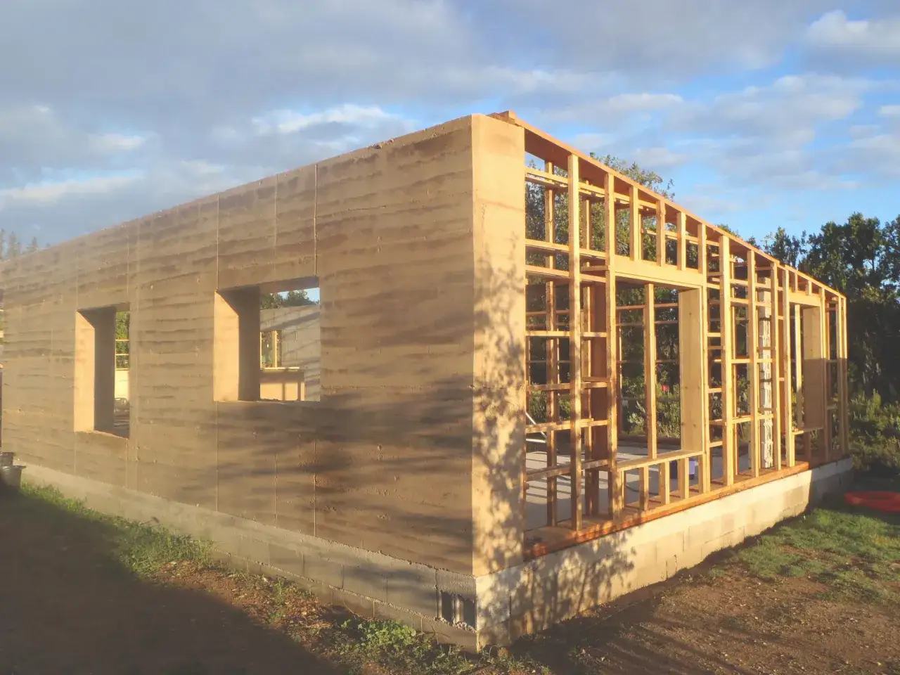 Construction d'une maison terre crue aux murs épais et texturés, avec une ossature bois visible pour la partie avant.