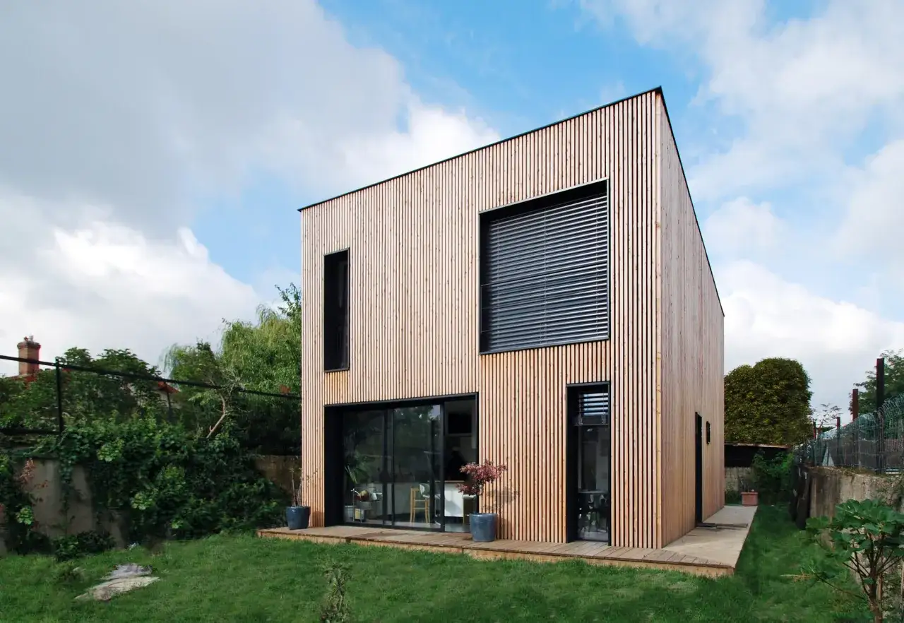 Maison de l'avenir prix : une construction moderne en bois avec de grandes baies vitrées, un jardin verdoyant et un ciel bleu.