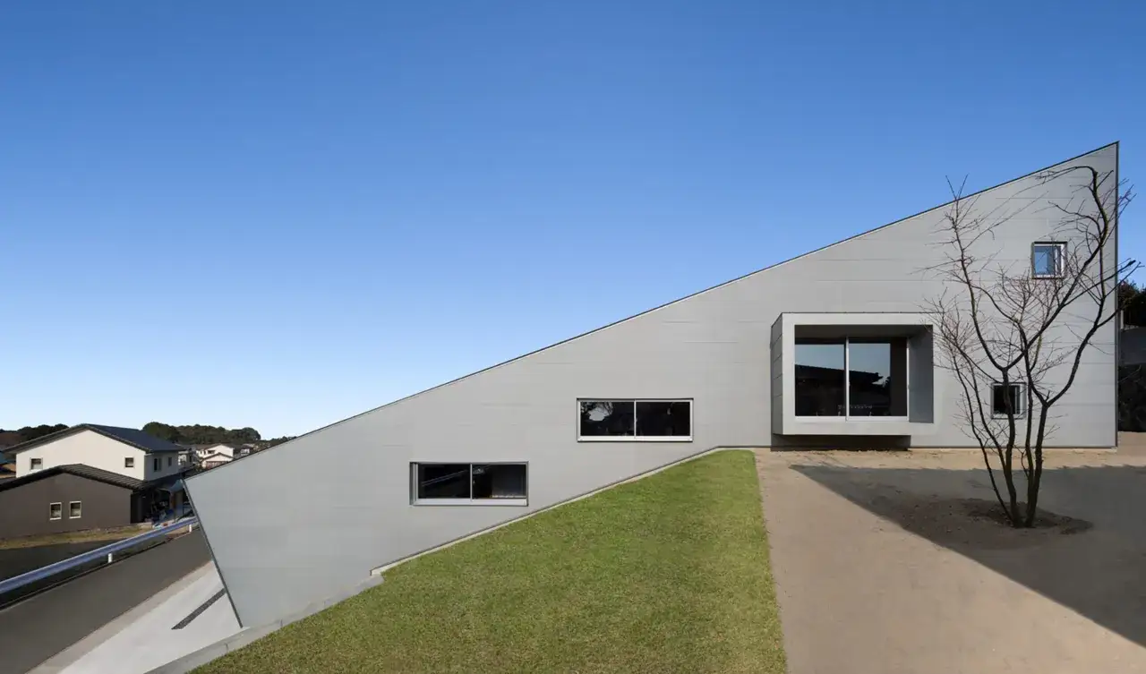 Maison moderne sur un terrain en pente raide, avec un toit incliné spectaculaire et de grandes fenêtres.