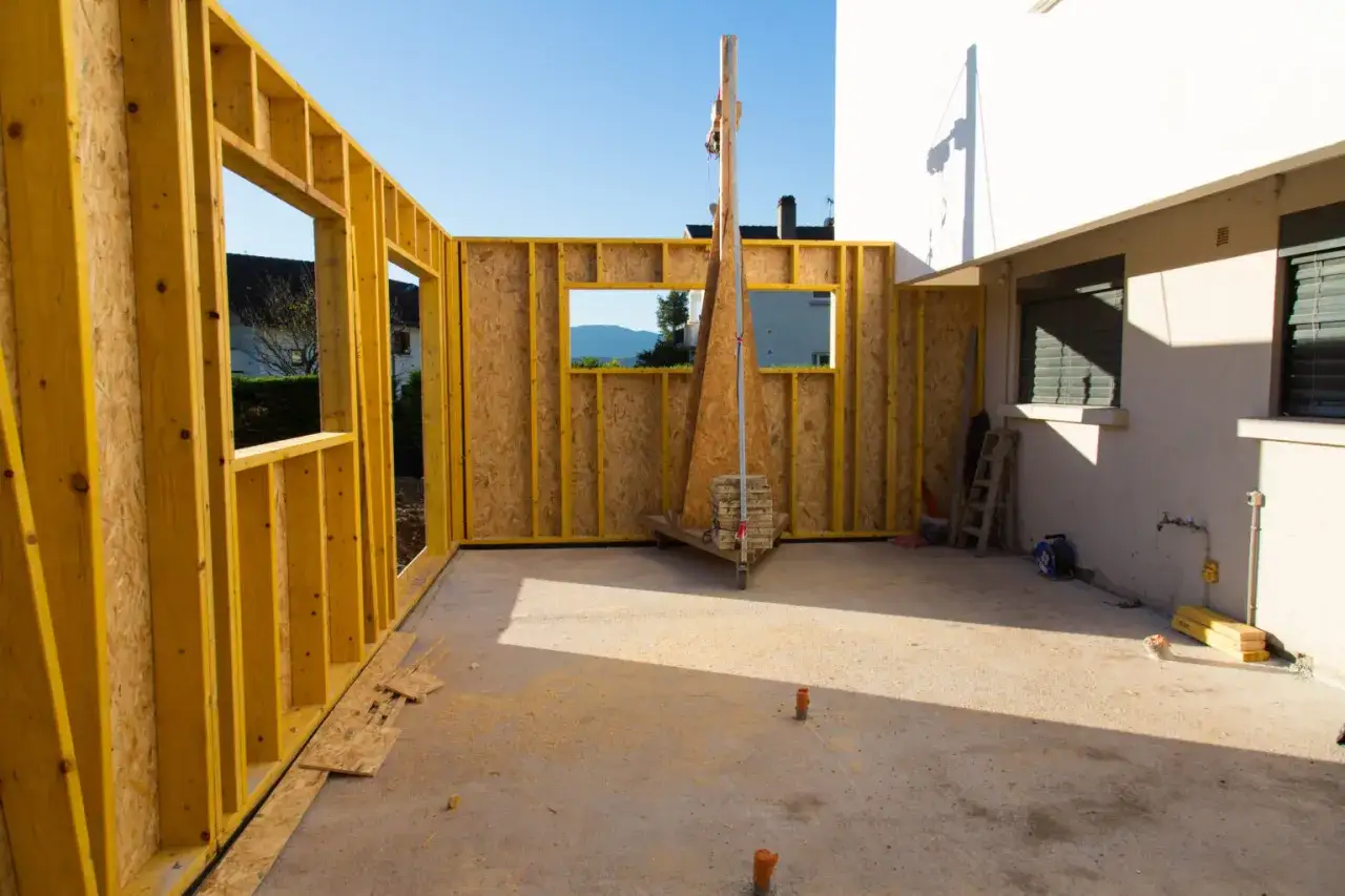 Structure en bois pour agrandir une maison. Le chantier est en cours, avec des murs en OSB et des ouvertures pour les fenêtres.