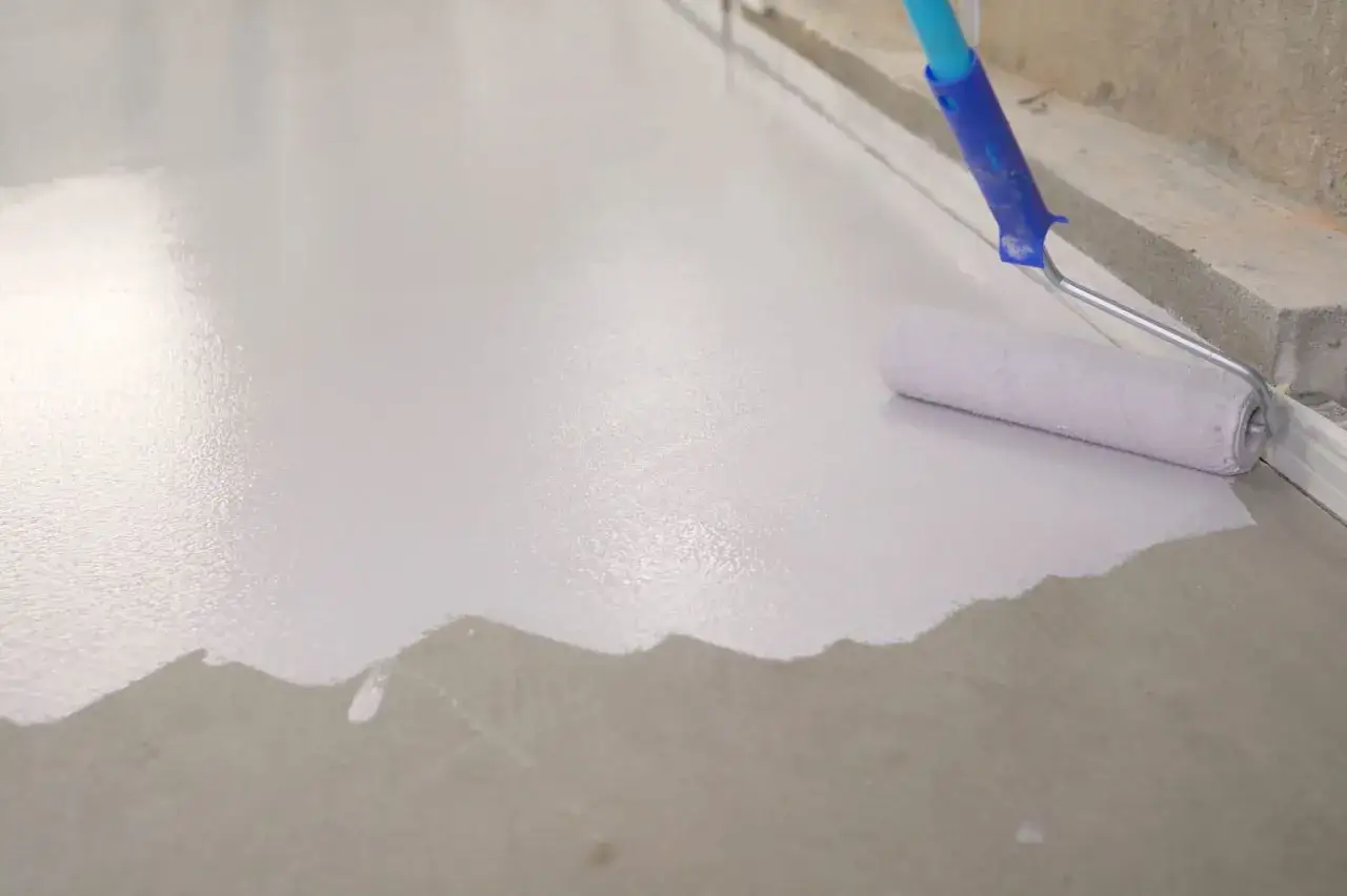 Application d'une peinture grise sur un sol de garage avec un rouleau. Le travail progresse, transformant la surface.