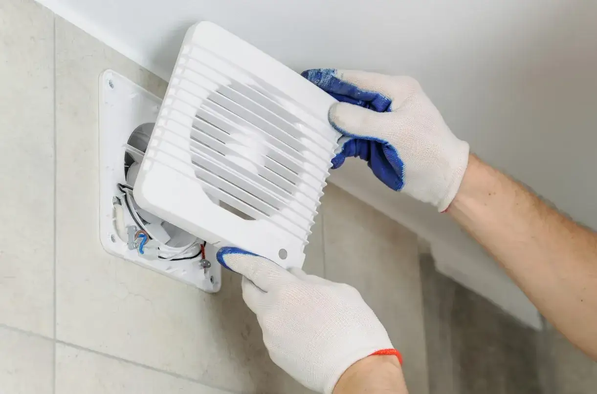 Mains de gants blancs ajustant un VMC qui fait du bruit. Installation d'un nouveau ventilateur pour plus de silence.