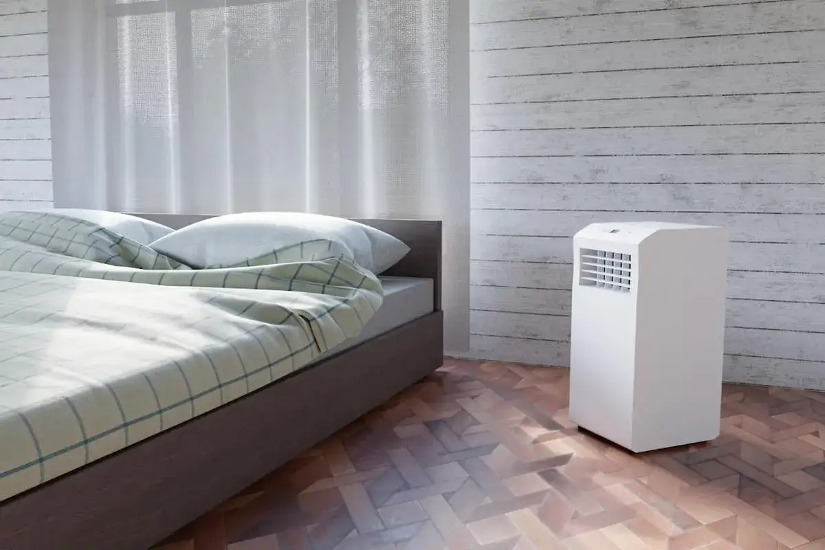 Un syst&egrave;me split sans &eacute;vacuation blanc, discret, dans une chambre avec un lit douillet et des rideaux l&eacute;gers.