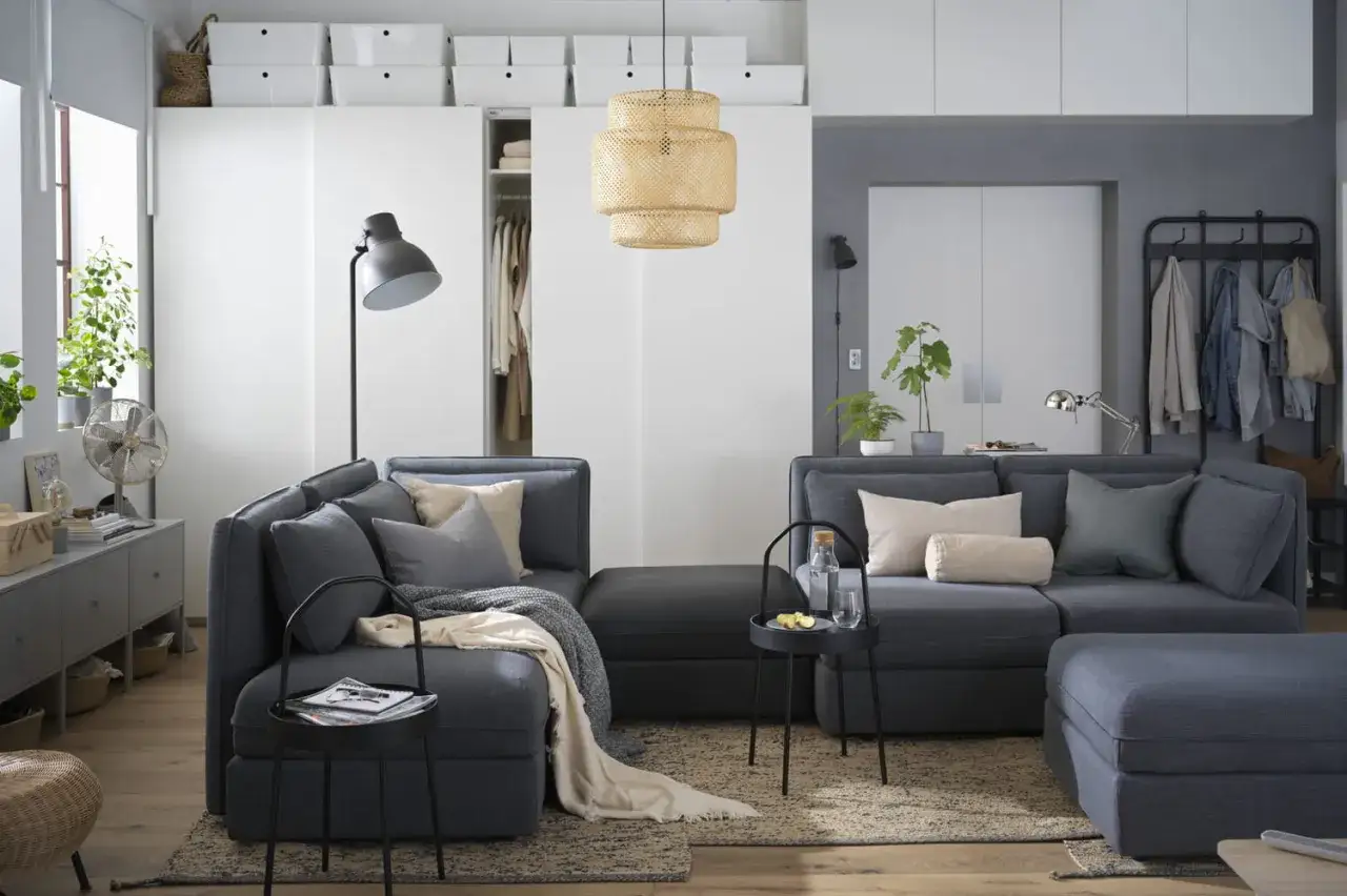 Comment am&eacute;nager un salon en L : un canap&eacute; d'angle gris, des coussins douillets, une table basse et des rangements astucieux pour un espace cosy.