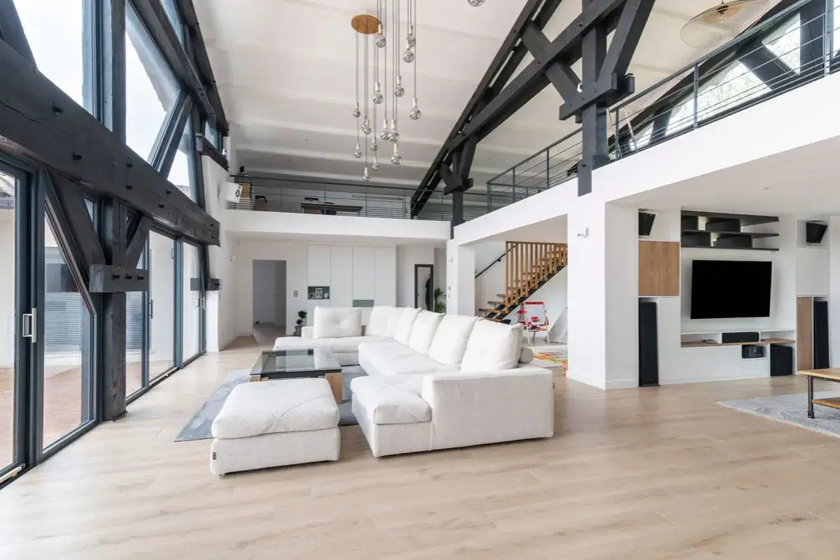 Salon moderne avec poutres apparentes, canapé blanc, escalier en bois. Le cout rénovation maison est élevé pour un tel espace.