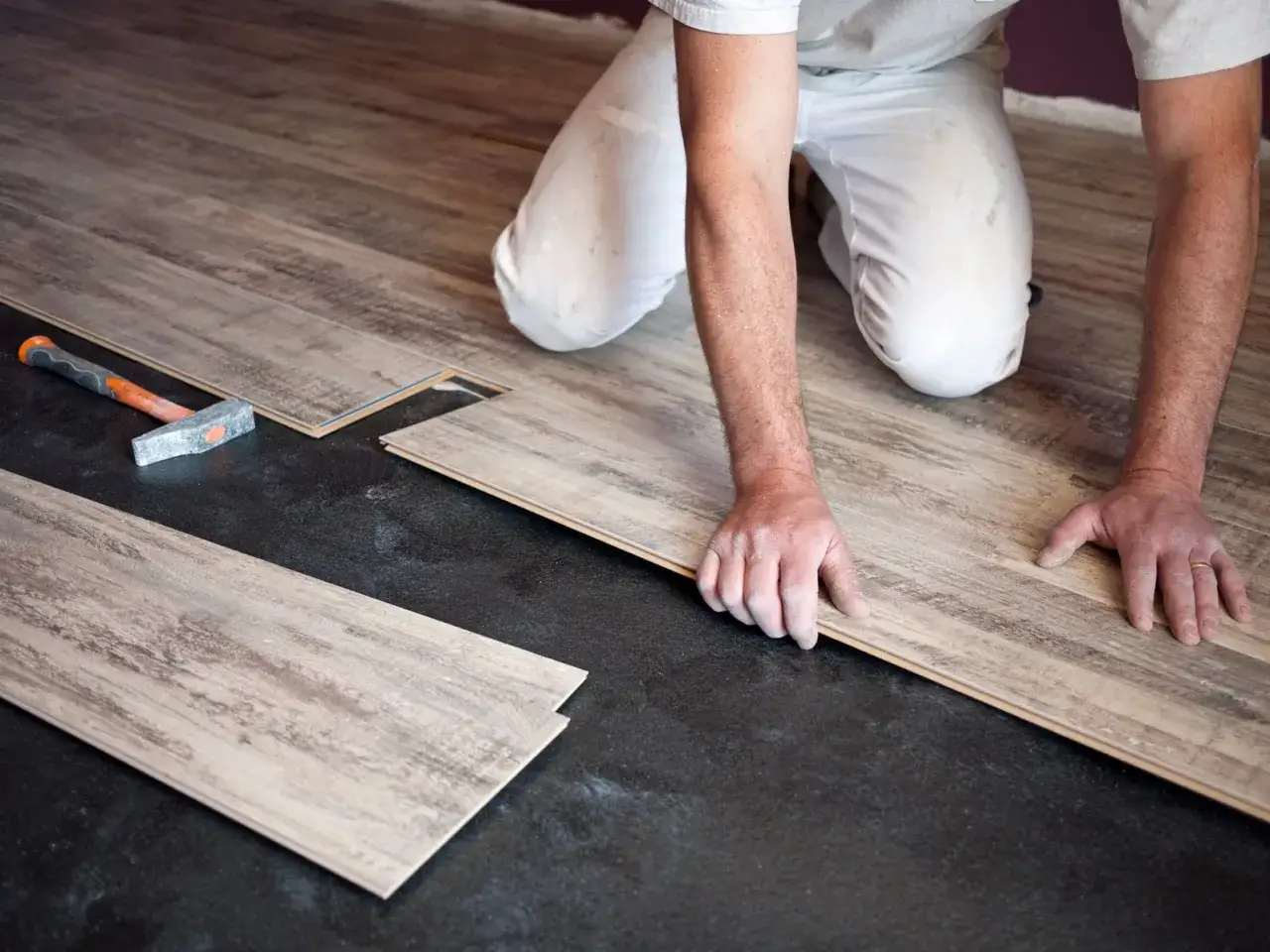 Pose de parquet flottant : un artisan installe des lames de bois sur un sol noir. Le prix de pose est un facteur clé pour ce type de revêtement.