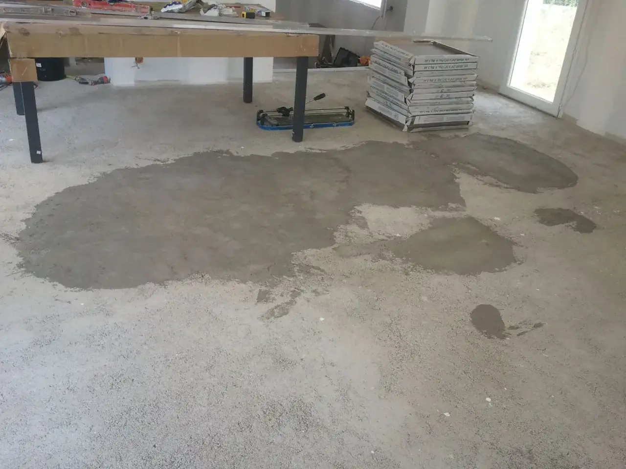 Préparation du sol pour le pose carrelage 60x60. Ciment frais étalé sur le béton brut, avec des boîtes de carreaux empilées à droite.