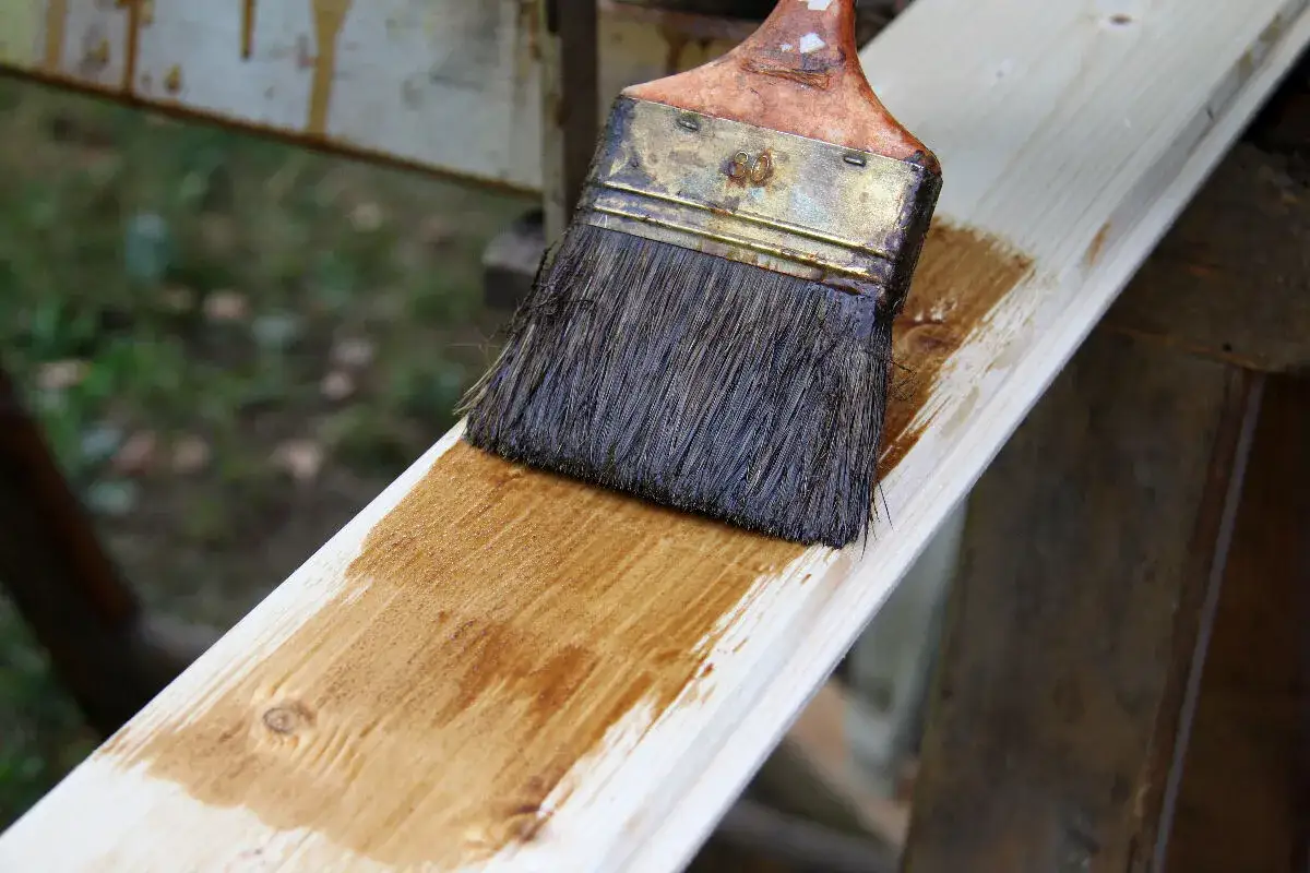 Application d'une lasure bois pour un avant-après visible. La brosse dépose une couche protectrice sur le bois brut.
