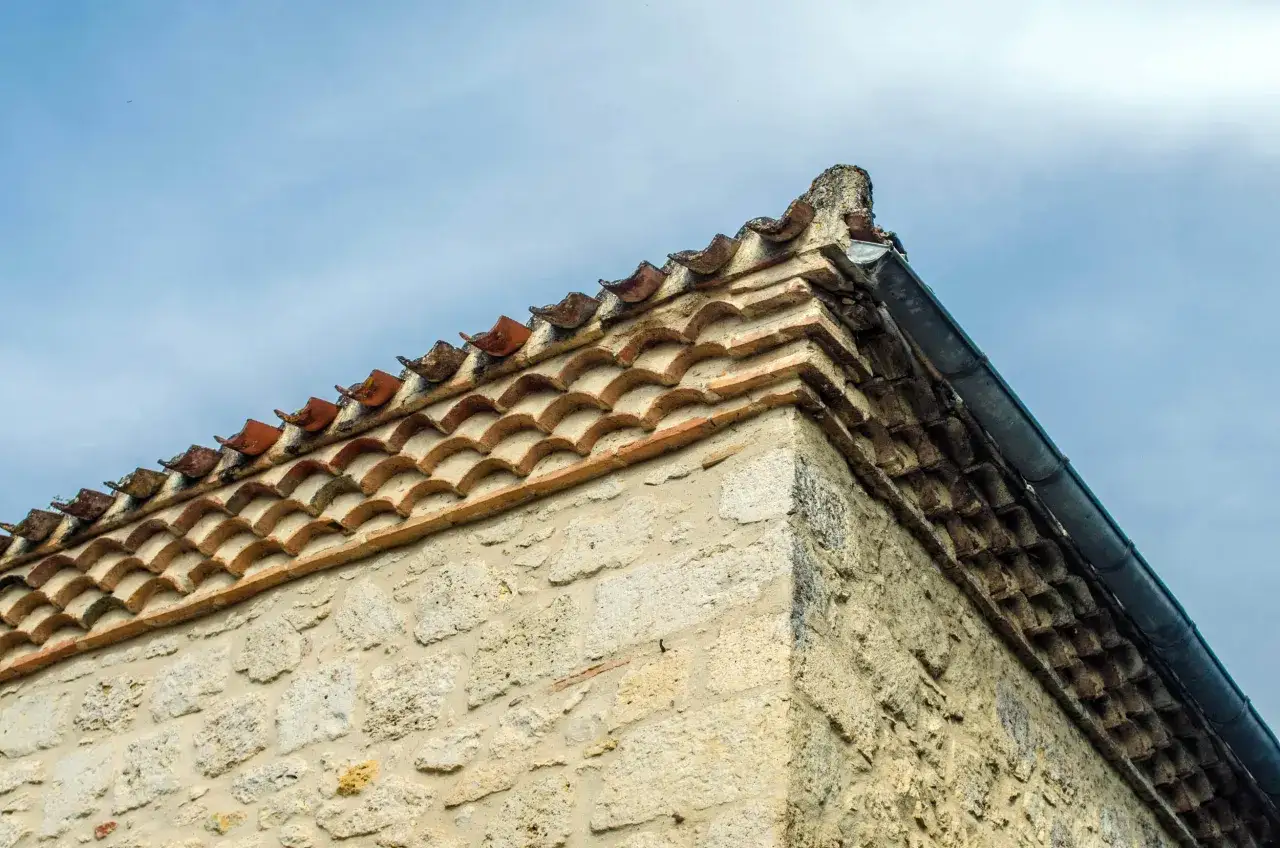 Le coin d'une maison provençale avec ses tuiles anciennes et son mur de pierres sous un ciel bleu.