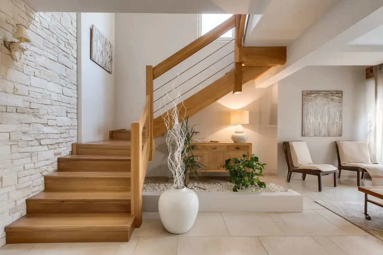 Escalier en bois clair, parfait pour une restauration. Un mur en pierre blanche et une décoration zen complètent l'ensemble.