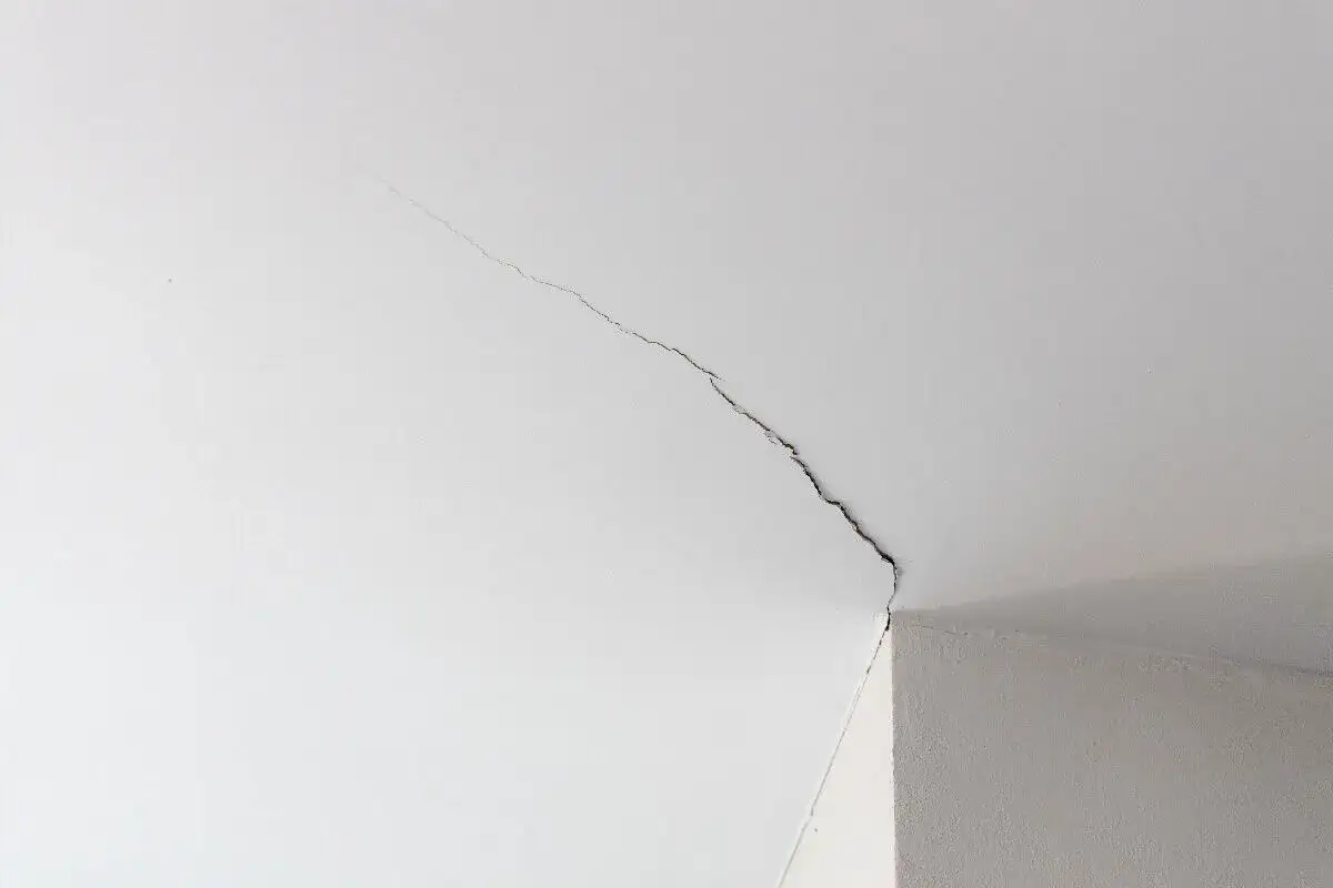 Une longue fissure traverse le plafond blanc, s'étendant d'un coin à l'autre, signalant un problème structurel.
