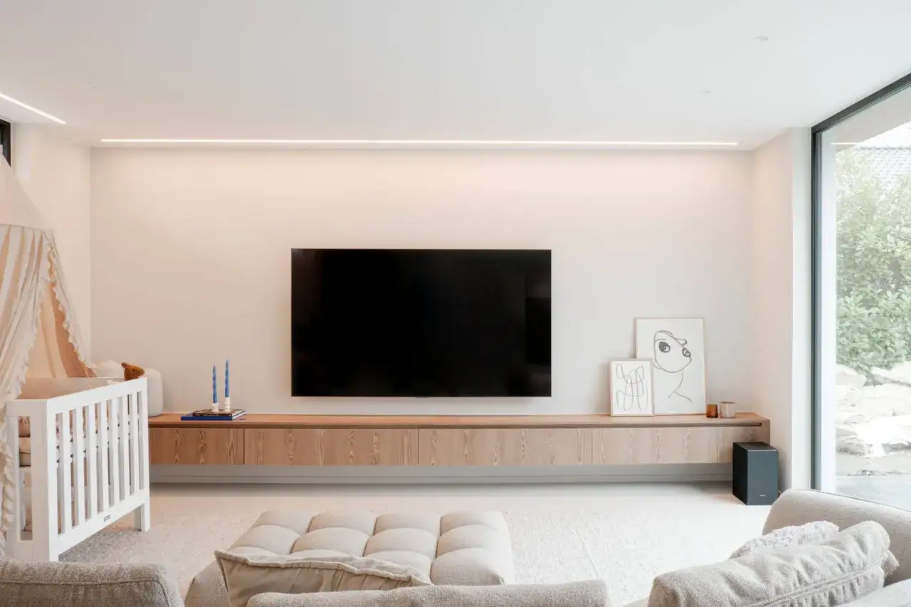 Salon moderne avec meuble suspendu en bois clair, t&eacute;l&eacute;vision, berceau et canap&eacute;. La hauteur du meuble suspendu salon est id&eacute;ale pour le rangement.