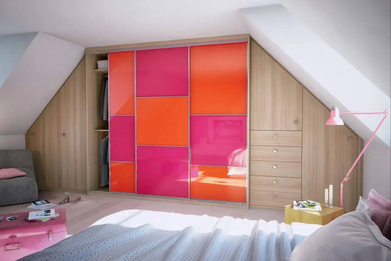 Am&eacute;nagement d'un dressing sous pente avec portes coulissantes color&eacute;es et rangements en bois.