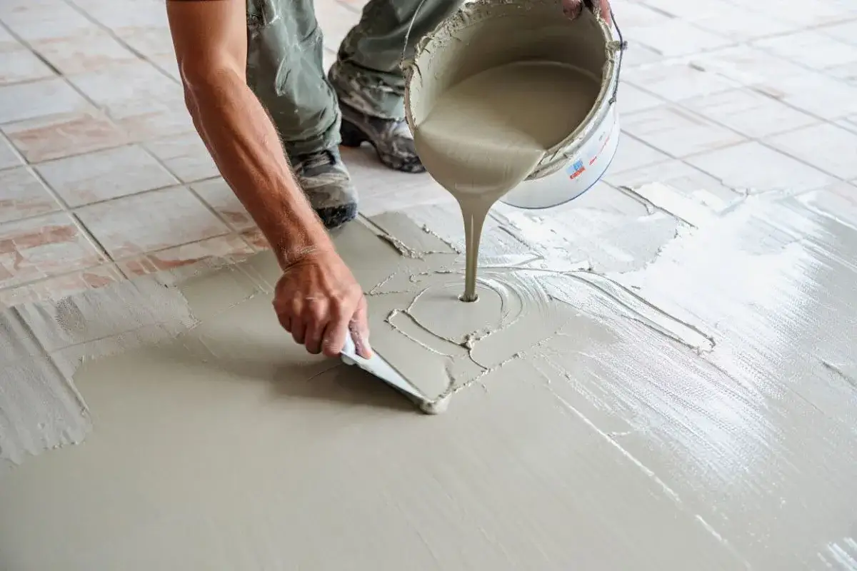 Application de béton ciré sur carrelage. Un ouvrier étale le produit avec une spatule, transformant le sol.