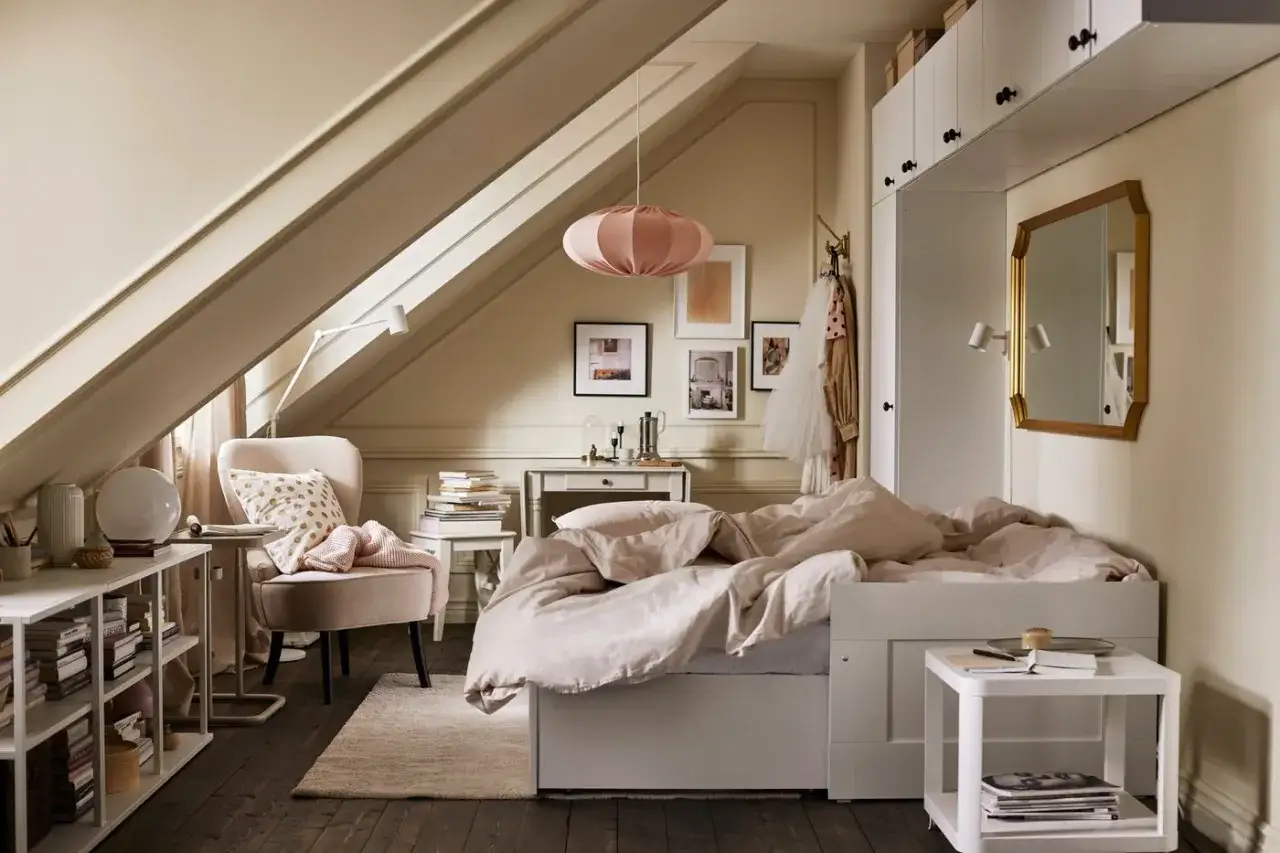 Chambre sous comble très bas, avec lit douillet, fauteuil cosy, étagères et miroir doré.