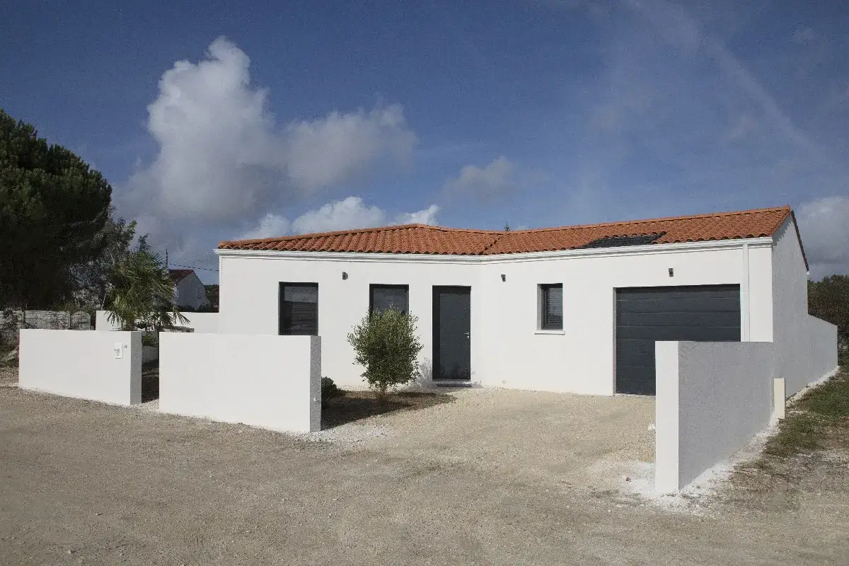 Une maison pavillonnaire moderne aux murs blancs et au toit de tuiles rouges, avec un garage gris et des murets bas.
