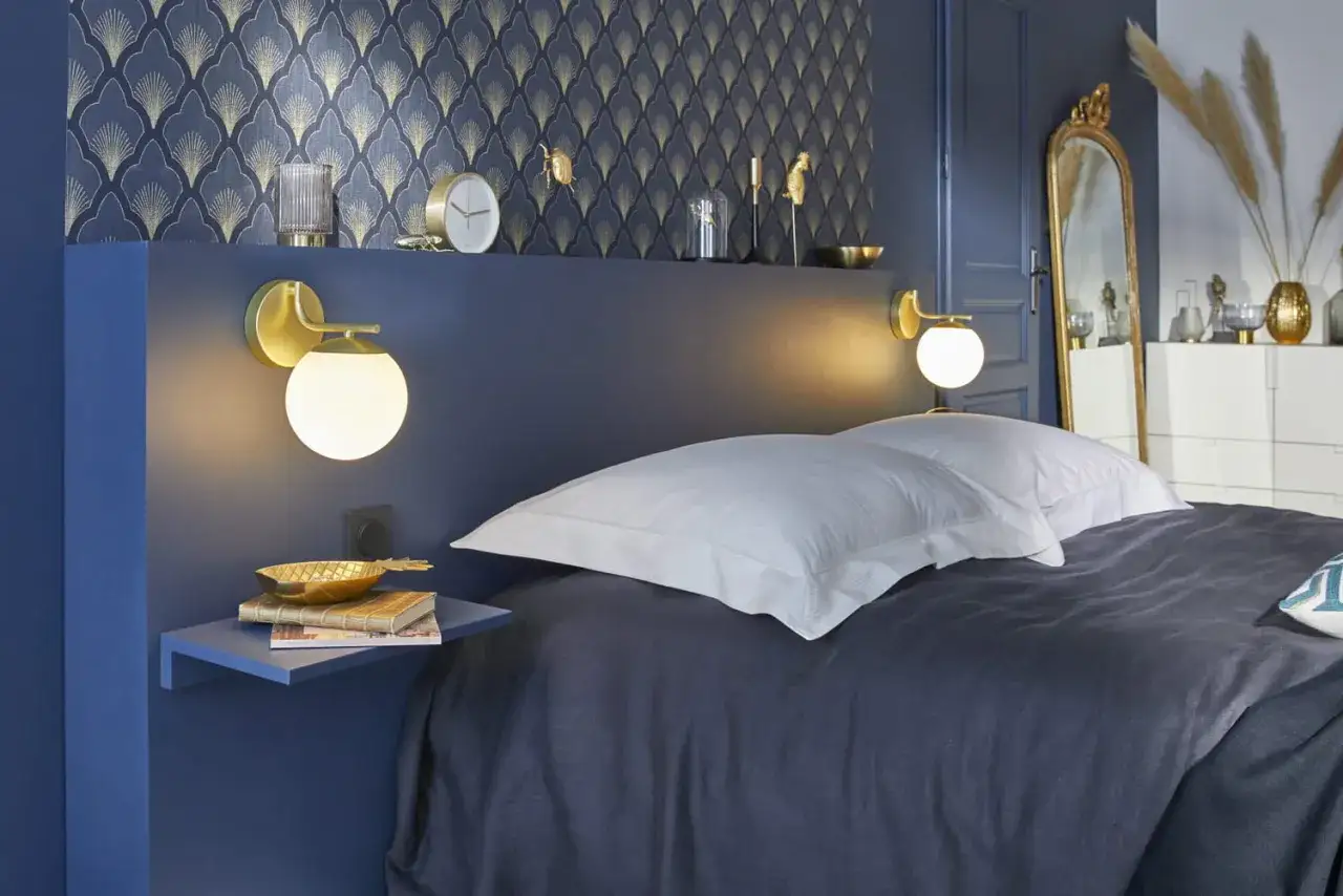 Le bleu nuit et le doré, une couleur conseillée pour une chambre élégante. Un lit douillet, des appliques murales modernes.
