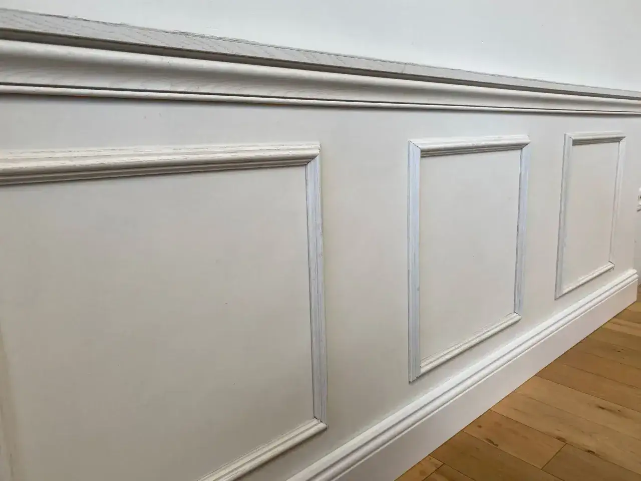 Soubassement de couloir avec moulures &eacute;l&eacute;gantes. Le bois clair du parquet contraste avec le blanc des panneaux muraux.