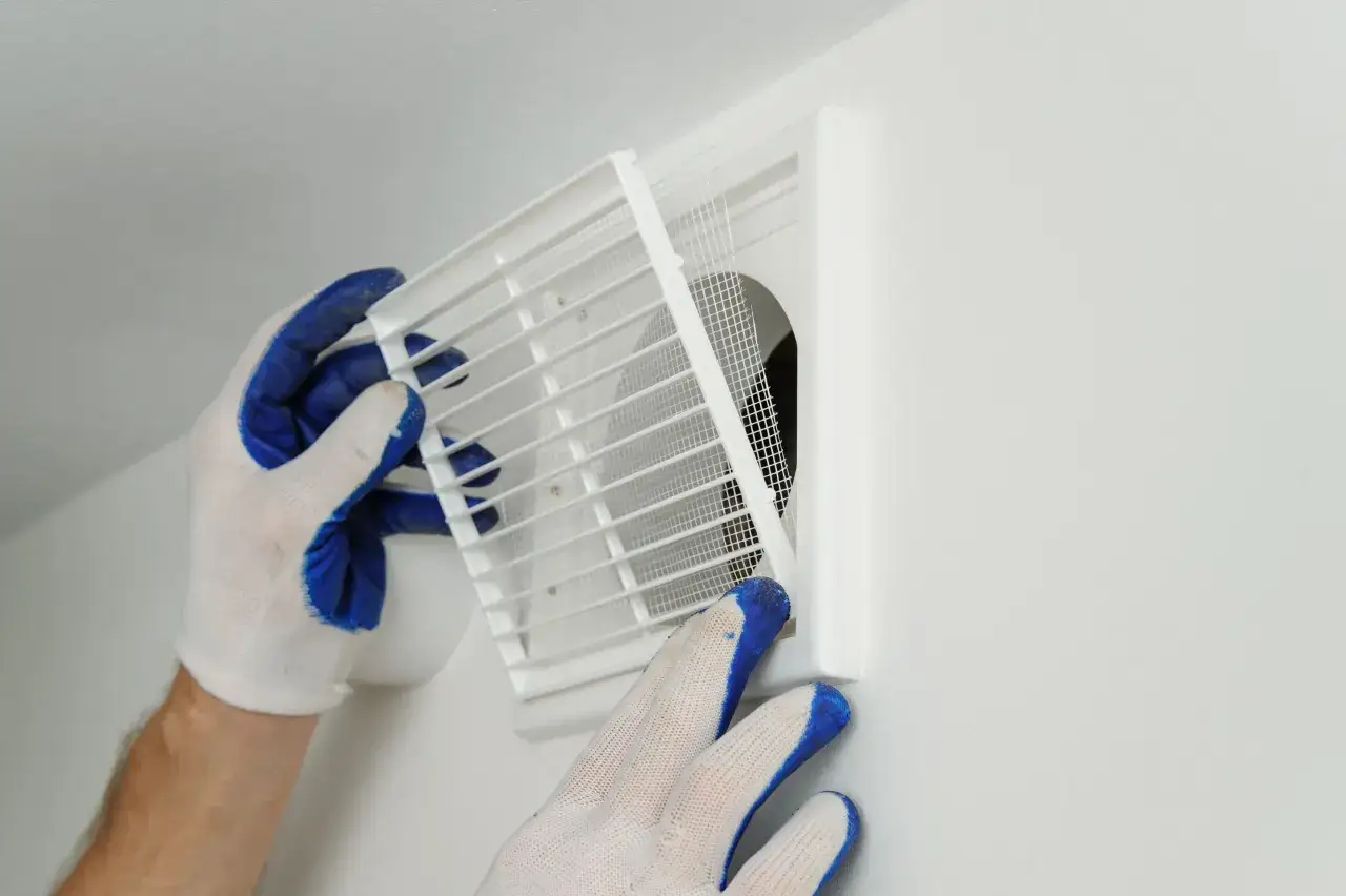 Mains d'un installateur de VMC ajustant une grille de ventilation blanche sur un mur.