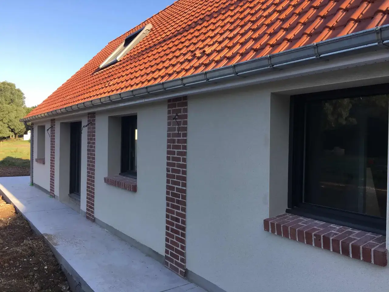 Comment cacher un vilain mur extérieur : des bandes de briques rouges ornent le crépi clair d'une maison neuve, ajoutant du cachet.