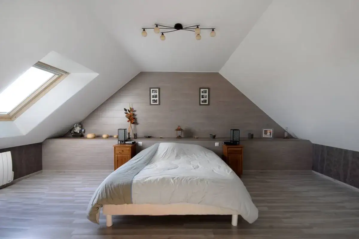 Douillette chambre mansardée avec un grand lit, une lucarne et une décoration murale en bois.
