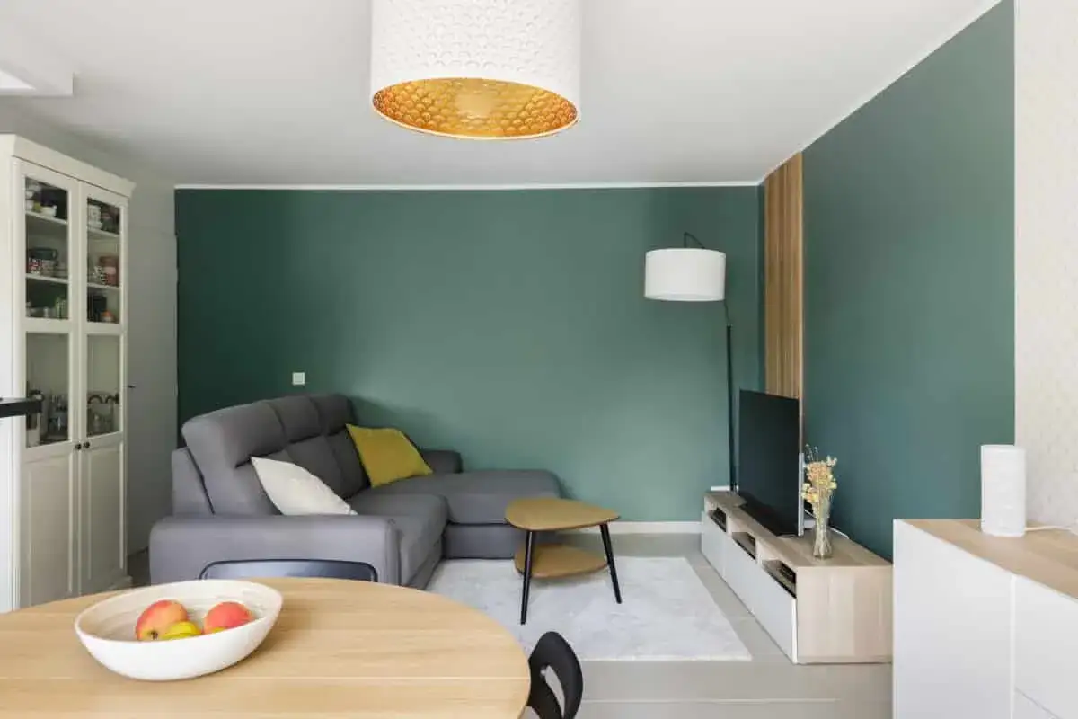 Salon moderne avec mur vert, canapé gris, table basse et meuble TV. Estimation du prix pour peindre une chambre de 12m2.
