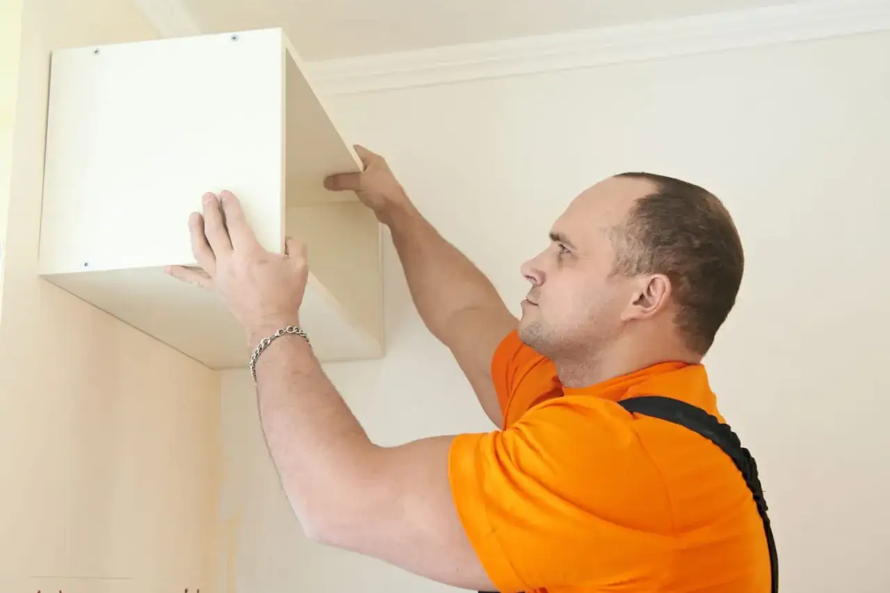 Un homme installe une étagère murale. Il faut bien choisir les fixations pour fixer meuble lourd sur placo.