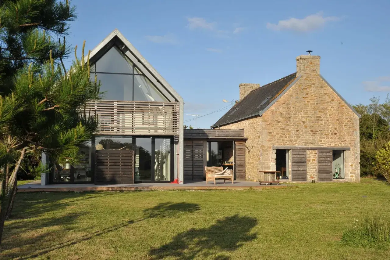 Une grange rénovée allie pierre ancienne et design moderne, avec une façade vitrée spectaculaire et une terrasse en bois.