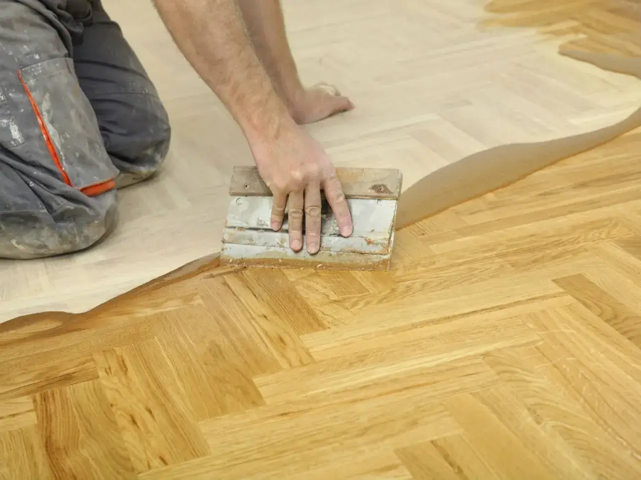 Un artisan applique un produit sur un parquet en chevrons. Une étape essentielle pour la réparation parquet.