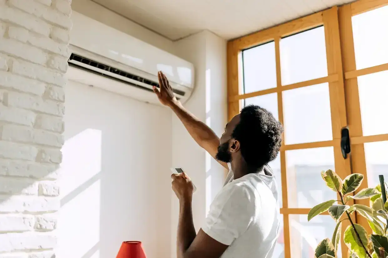 Un homme v&eacute;rifie sa climatisation murale, pr&ecirc;t &agrave; recharger clim maison pour un confort optimal.
