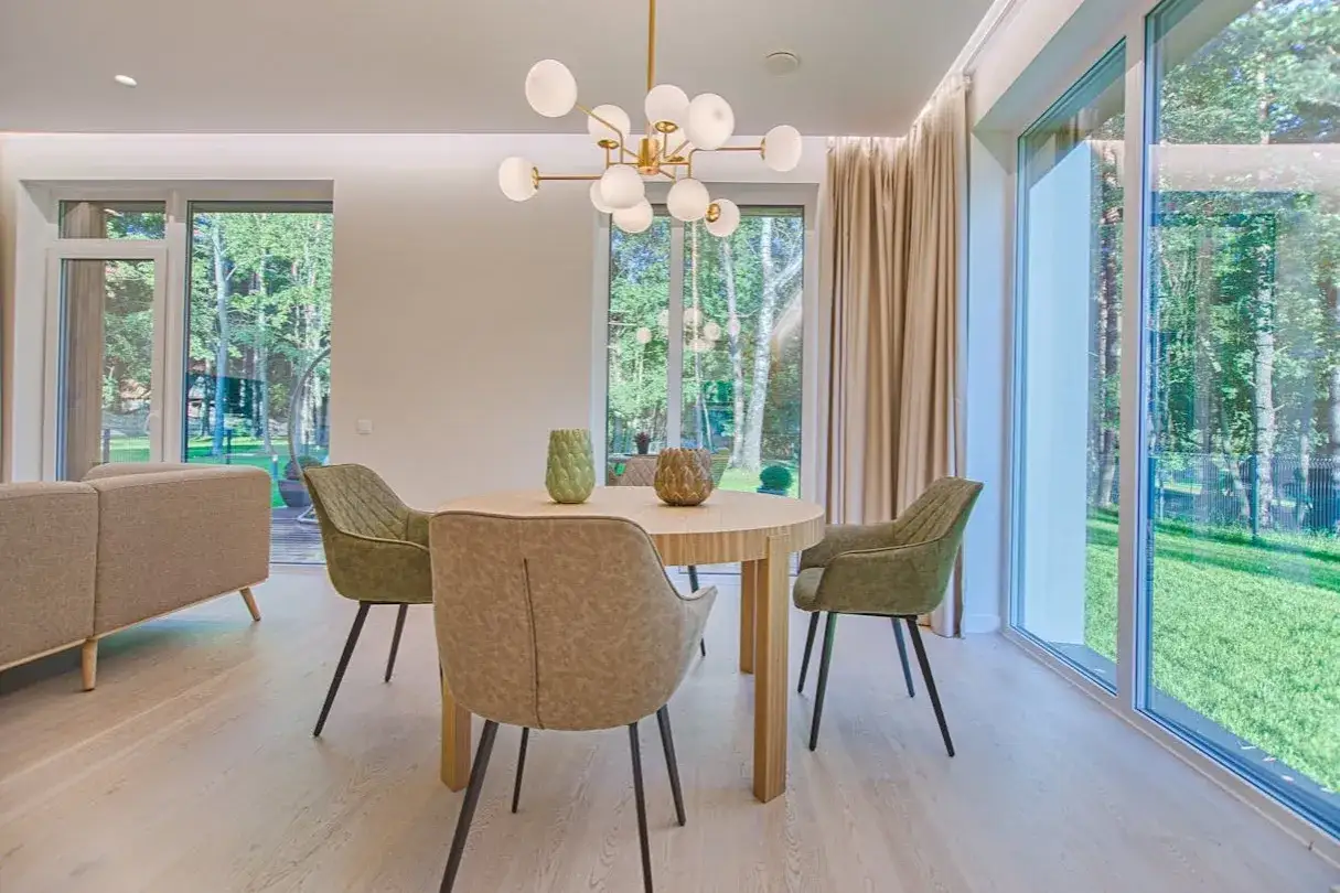 &Eacute;clairage salle &agrave; manger sans plafonnier : suspension moderne au-dessus d'une table ronde, entour&eacute;e de chaises vertes. Lumi&egrave;re naturelle abondante.