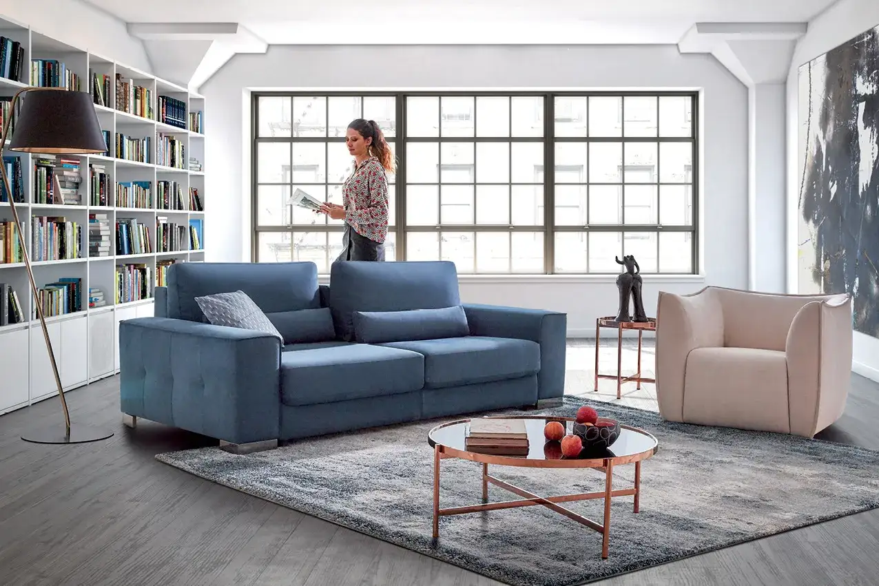 Canap&eacute; bleu profond, couleur canap&eacute; moins salissant, dans un salon moderne avec biblioth&egrave;que et fauteuil beige.