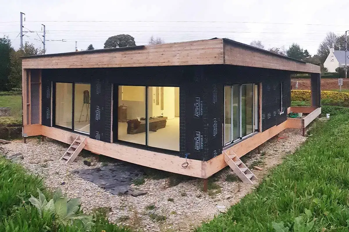 Maison en carton en construction, avec de grandes baies vitrées et une structure en bois.