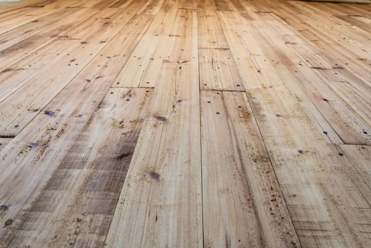Planches de bois clair, usées et clouées, évoquant un parquet qui craque sous les pieds.