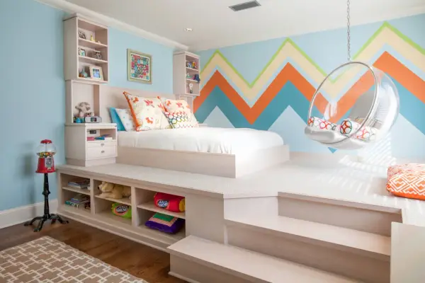 Chambre fille petit espace avec lit sur estrade, rangements intégrés, fauteuil bulle et mur géométrique coloré.