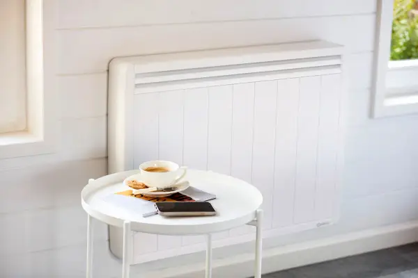 Un radiateur blanc moderne, idéal pour le chauffage maison neuve, avec une tasse de café et des magazines sur une table d'appoint.