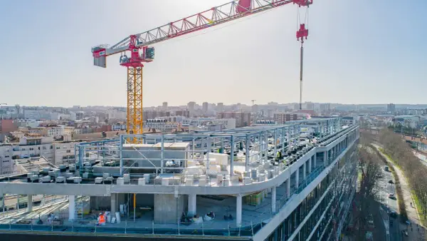 Grue de chantier sur un bâtiment en construction rapide, avec une ville en arrière-plan.