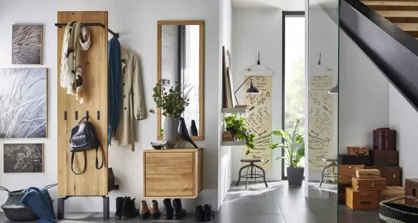 Une entrée dans un salon moderne avec un portant en bois, des manteaux, un sac à dos, des tableaux et une étagère avec des plantes.