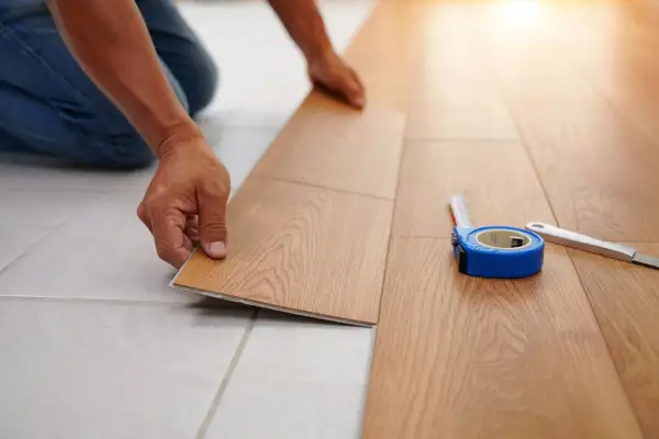 Pose d'un nouveau revêtement de sol imitation bois, une solution pour niveler un sol sans ragréage. Un mètre ruban et un cutter sont à proximité.
