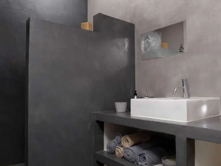 Salle de bain moderne avec murs en béton ciré. Une douche sans joint, un lavabo rectangulaire et des serviettes pliées créent une ambiance épurée.