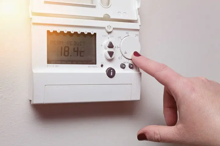 Main d'une femme ajustant un cee thermostat connecté affichant 18.4°C.