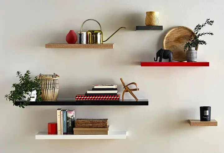 Étagères flottantes décorées : plante, arrosoir doré, livres, éléphant, bougie. La hauteur entre étagère varie pour un design dynamique.