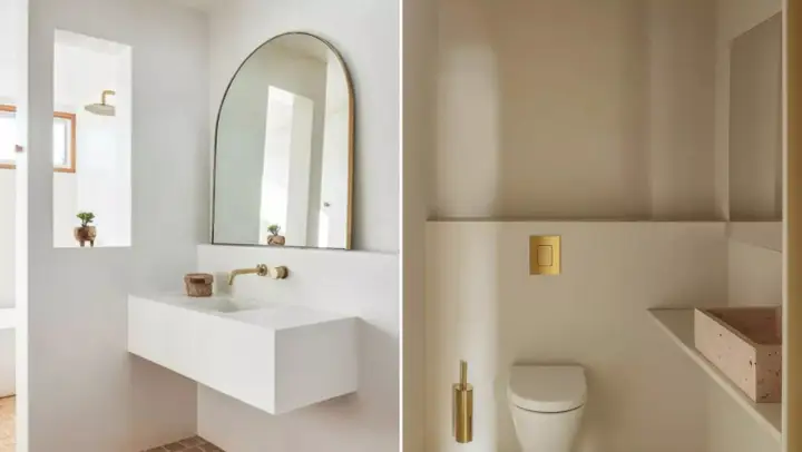 Idées pour décorer ses toilettes : un lavabo suspendu blanc, un miroir arche doré, une chasse d'eau dorée et une brosse WC assortie.
