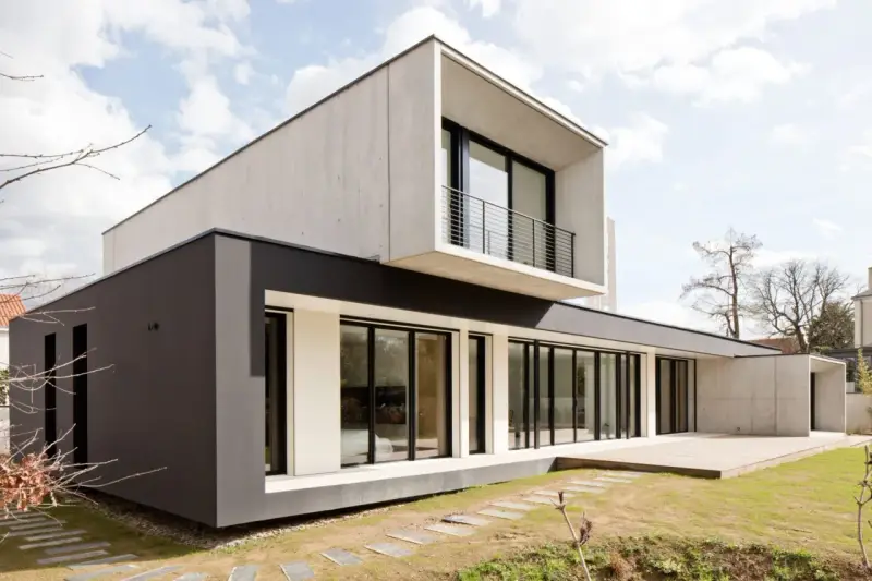 Maison moderne avec façade en béton et bardage sombre, grande baie vitrée et terrasse en bois.