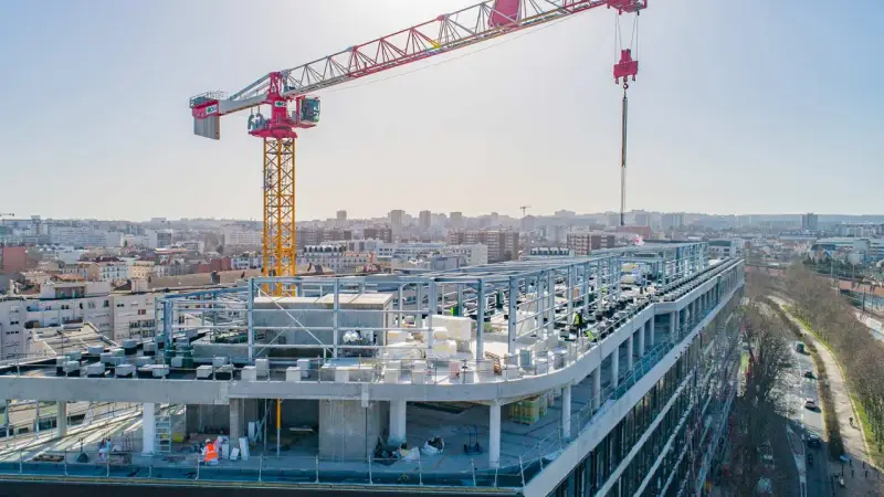 Grue de chantier sur un bâtiment en construction rapide, avec une ville en arrière-plan.